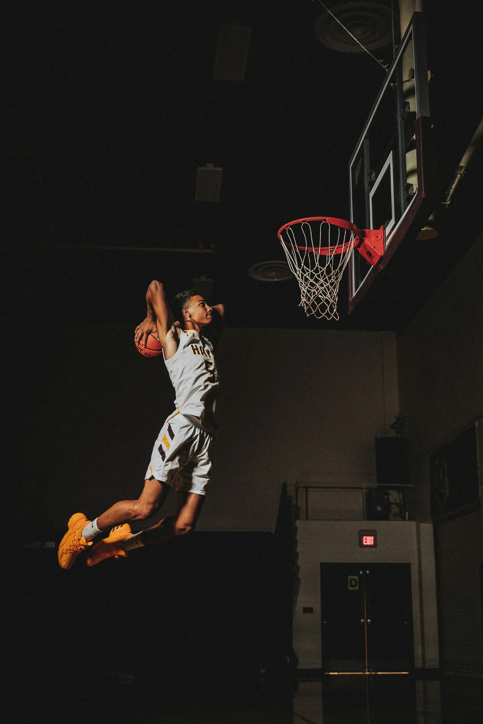 A basketball player jumping toward the hoop in a dark gym