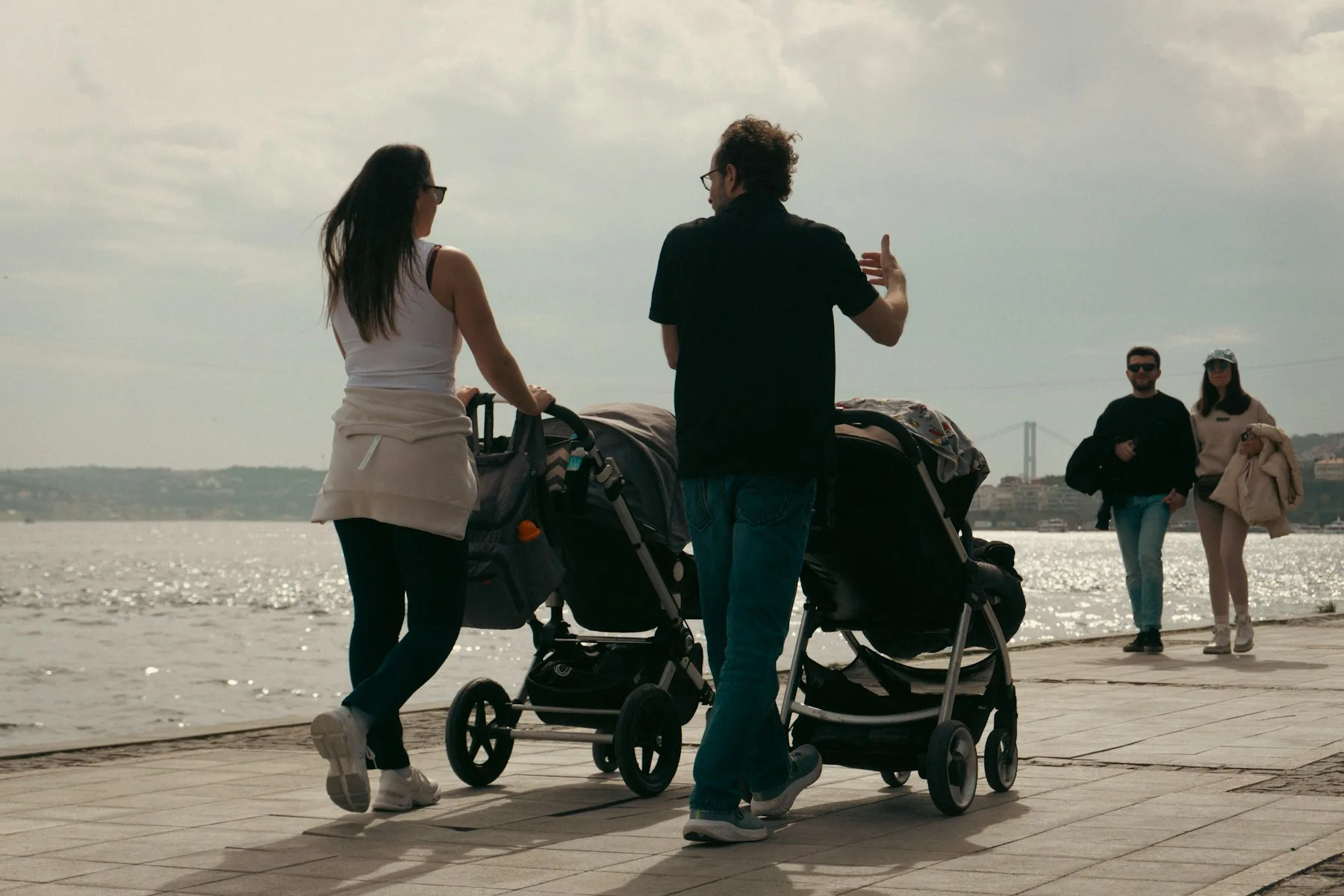 Parents walking with two baby strollers by the water