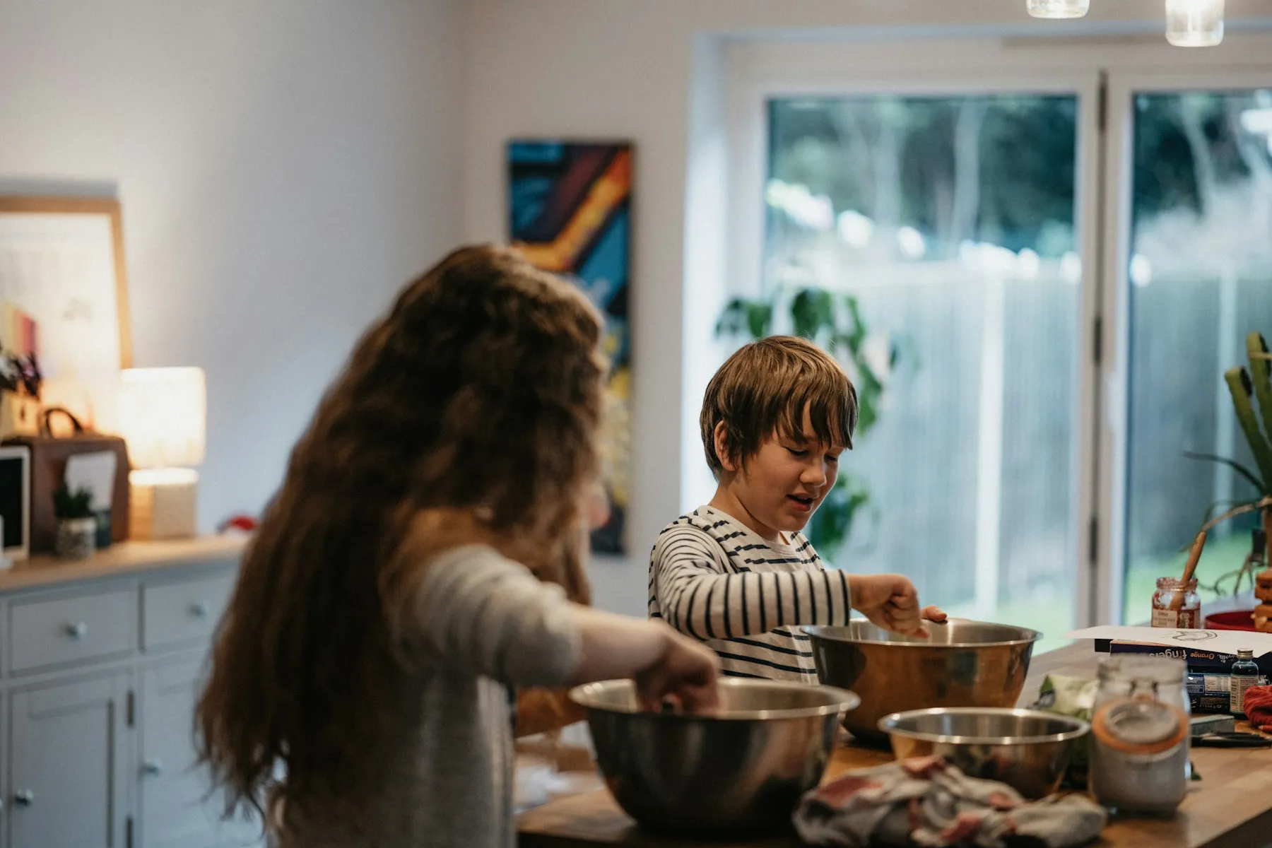 Two children mixing ingredients in a lived-in family kitchen