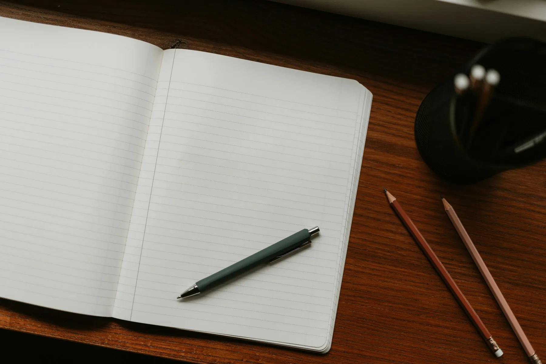 An open lined notebook with a pen and pencils on a wooden desk